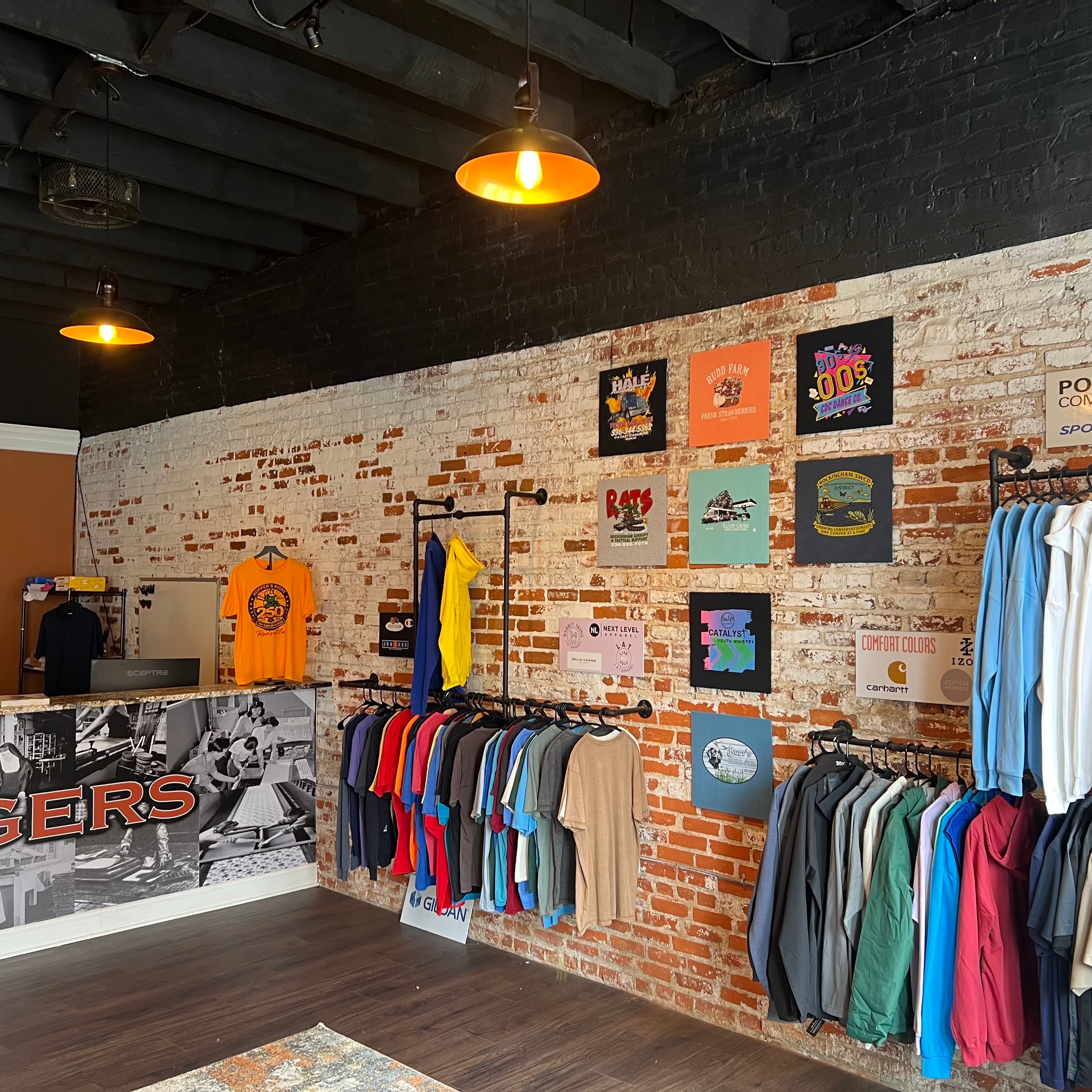 Screen Print Plus shop interior — exposed brick wall with custom printed t-shirts on display